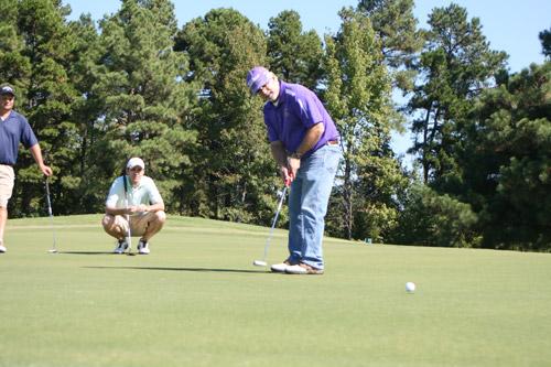 Father John Marconi, pastor of St. Joseph Church in Conway, takes his putt as fellow golfers Matt Mallett, business manager at St. Joseph, and Randy Mayor watch. (Aprille Hanson photo)