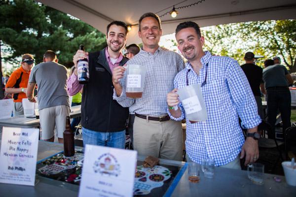 St. Raphael parishioners and hobby brewers Adam White and Rob Philips enjoy a bit of friendly competition with friend Tom Haugh as they show off their home brews. (Travis McAfee photo)