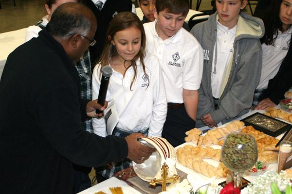 Father Y.C., pastor at St. John Church, explains the significance of a turban  from his native India that he placed on the St. Joseph altar, to fifth graders Helen Van Wagner (left), Matthew Bozeman, Mary Drakes and Eva LaCombe. Items from various cultures were placed on the altar for parishioners to share about their heritage. (Aprille Hanson photo)