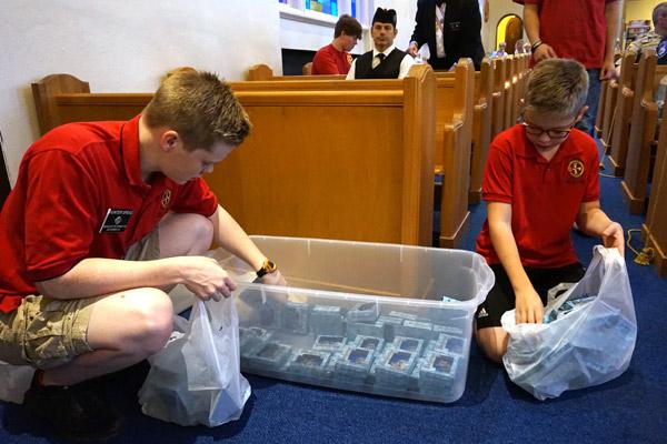 Hunter Speas, 16, (left) and his younger brother Peyton, 11, bag the blessed St. Michael visor medals that will be placed in first responder vehicles throughout Garland County. The two are members of the Columbian Squires Circle 5700 which organized the event. (Aprille Hanson photo)  