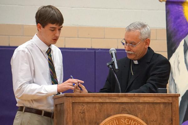 Bishop Anthony B. Taylor passes the pen along to senior Thomas DePrez to sign his letter of intent to discern his priestly calling as a diocesan seminarian this fall. (Aprille Hanson photo)