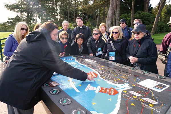 A tour guide at the American Cemetery in Normandy shows a map April 7 of where American forces came ashore on D-Day 75 years ago. After a short tour, the pilgrims were allowed to walk the grounds of the cemetery where 9,387 Americans are buried. British and Canadian cemeteries are also located in the area. (Malea Hargett photo)