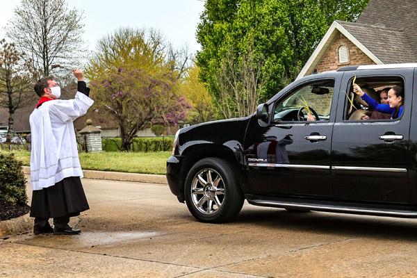 Pastor Father Jason Tyler blesses the palms as parishioners drive by April 5. After picking up their palms, members of St. Joseph Church drove around the church’s Fayetteville neighborhood in a procession to celebrate the holy day. (Robert Brady photo) (Not available for sale)