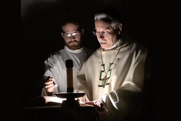Deacon Joseph Friend holds a flashlight for Bishop Anthony B. Taylor as he begins the Easter Vigil Mass April 11 in the dark at the House of Formation in Little Rock. Bishop Taylor celebrated Holy Week Masses with seminarians and staff. (Pablo Quintana photo) (Not available for sale)