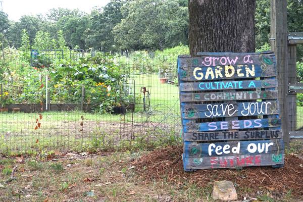 A sign rests against a tree near the community garden beds at St. Joseph Center of Arkansas in North Little Rock. Volunteers tend to the garden beds, a slice of agricultural life in the midst of an urban area.  (Aprille Hanson photo)