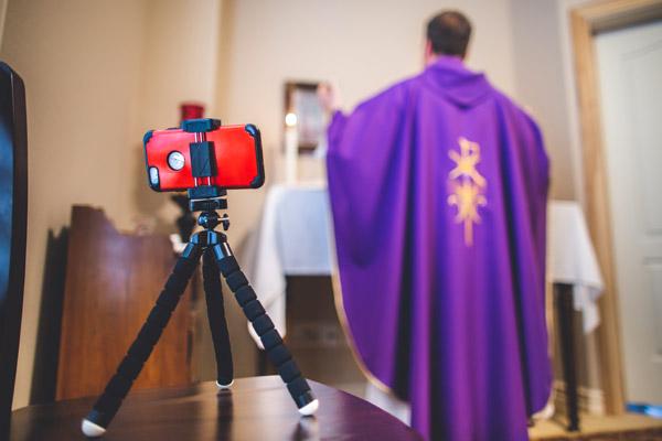 Early in the COVID-19 pandemic, Father Jason Tyler's smartphone and tripod help him livestream videos daily on Facebook to celebrate Mass for his parishioners and friends. He is seen here March 18 from his rectory chapel. (Travis McAfee photo, Arkansas Catholic file)