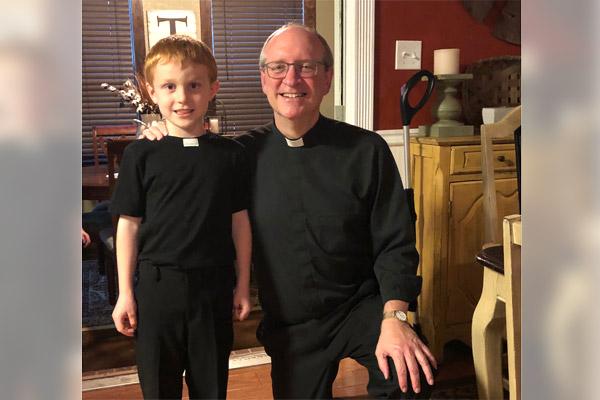 After his first Communion about two years ago, Owen Thompson, donning “priestly” attire, smiles with Father James West, who came over to the family’s Texarkana house to celebrate. Owen hopes to one day be a priest, thanks in part to Father West as a role model. (Courtesy Thompson family)