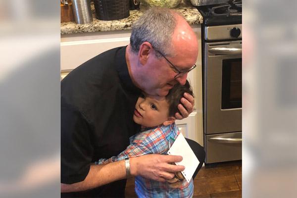Father James West hugs toddler Fletcher Engel, grandson of Greg and Brenda Engel in their Sherwood home in spring 2019. Brenda Engel said Father West, who died last year, was like a brother to her. (Courtesy Brenda Engel)