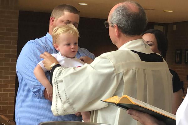 Father James West baptizes Grayson Engel, held by his father Austin Engel, at Immaculate Conception Church in North Little Rock in spring 2019. (Courtesy Brenda Engel)