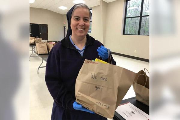 Sister Iliana Aponte, DC, smiles, holding a sack of homework to give to parents of students at St. Theresa School in Little Rock in spring 2020. Along with homework, the school gave food boxes in drive-thru events. (Courtesy Sister Iliana Aponte)