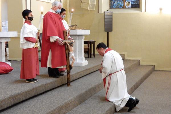Father George Sanders, pastor of St. John Church in Hot Springs, kneels before the cross on Good Friday April 2. The cross is held by Deacon Robert Wanless. (James Keary photo)