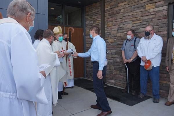 Greg Schluterman, an engineer for HFA in Bentonville who worked on the new St. Leo the Great University Parish in Russellville, hands architectural plans for the parish to Bishop Anthony B. Taylor during the dedication Mass April 14. (Aprille Hanson Spivey photo) 