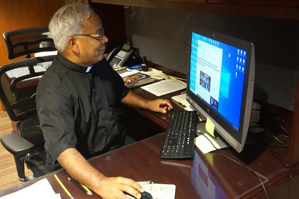 Father Aby Abraham, IMS, associate pastor at the Cathedral of St. Andrew in Little Rock, reads an India Times online article May 5 about the continuing COVID-19 crisis in his native India. (Aprille Hanson Spivey photo)