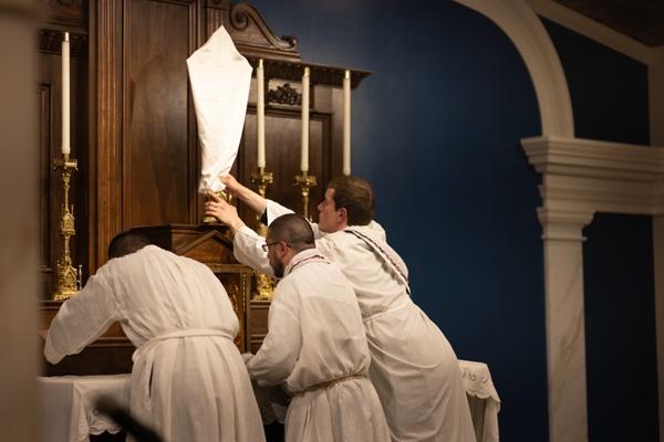 Two altar servers assist pastor Father Joshua Passo in covering the crucifix and stripping the altar at the end of Holy Thursday Mass April 14 at Our Lady of Sorrows Church in Springdale. Travis McAfee photo.
