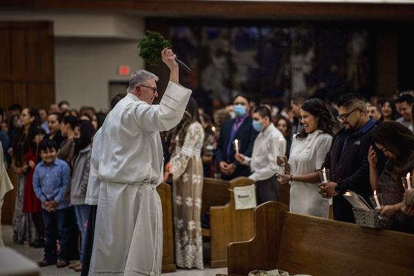 Pastor Father John Connell sprinkles holy water on parishioners after they renew their baptismal promises at the Easter Vigil April 16 at St. Raphael Church in Springdale. Travis McAfee photo.
