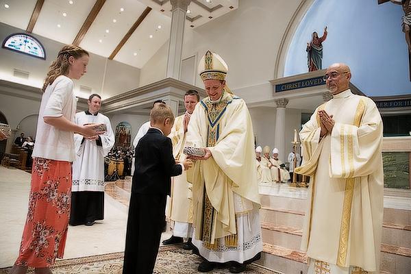 Bishop Erik Pohlmeier accepts the gifts from two of his godchildren  —  niece Rose Pohlmeier of Springfield, Va., and nephew Damien Pohlmeier of Fayetteville  —  during his episcopal ordination Mass July 22 in Jacksonville, Fla. (Bob Ocken)
