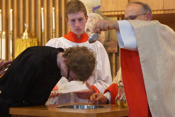 Father Norbert Rappold (photo above) pastor of St. Peter the Fisherman Church in Mountain Home, baptizes John Hargrove, 19, during Easter Vigil Mass March 30. Altar server Francis Kelly, 16, assists. (Aprille Hanson Spivey)